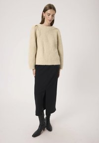 Beżowy sweter z dzianiny o strukturalnym wzorze, połączony z czarną spódnicą z rozcięciem po boku oraz czarnymi kozakami do kolan.