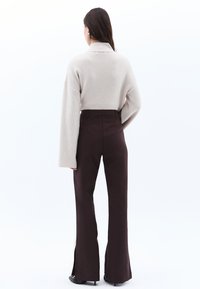 Beige geribde gebreide trui met wijde mouwen, gecombineerd met hooggetailleerde bruine flared broek met zijsplitten en een getailleerd ontwerp.