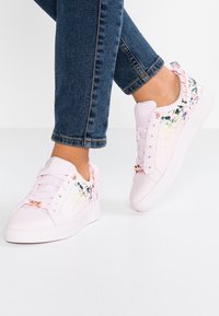 Baskets roses avec une finition en cuir lisse, motif floral sur les côtés et accents de ruban décoratif sur le talon. Semelle en caoutchouc blanche.