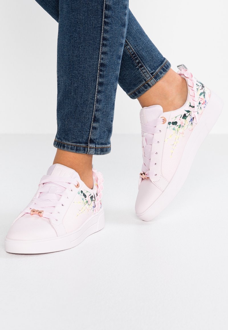 Baskets roses avec une finition en cuir lisse, motif floral sur les côtés et accents de ruban décoratif sur le talon. Semelle en caoutchouc blanche.