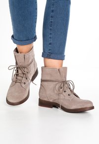 Suede ankle boots in light gray with lace-up front, stitched detail, and low brown heel. Worn with rolled blue jeans.