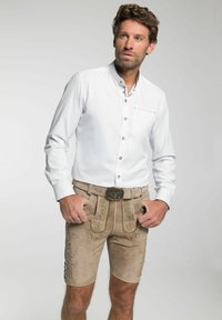Witte lange mouwen shirt met knoopdetails, gecombineerd met tan suede shorts met geborduurde bloempatronen en een decoratieve riemgesp.