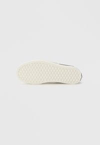 Svart sneaker sula med en texturerad vit gummibotten, som har ett diamantmönster för grepp. Släta och rundade kanter.