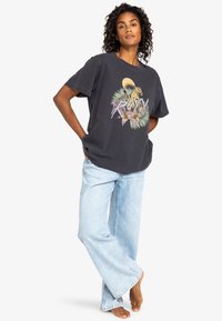 T-shirt in cotone grigio scuro con una grafica colorata di leopardo e piante. Abbinato a jeans larghi blu sbiaditi, creando un look rilassato.