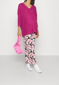 Person som bär en magenta stickad tröja, svart blommig kjol med rosa och vita blommor, vita sneakers och håller en rosa handväska.