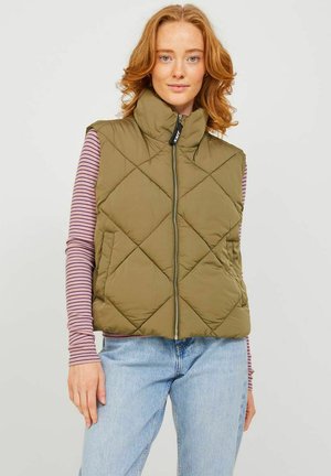 Gilet matelassé vert olive avec un motif en losanges, col haut et fermeture zippée à l'avant. Superposé avec une chemise à rayures à manches longues et un jean bleu.