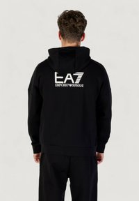 Schwarzer Kapuzenpullover mit einem weißen Logo "EA7 EMPORIO ARMANI" auf dem Rücken, aus Baumwolle gefertigt, mit lockerer Passform und gerippten Bündchen.