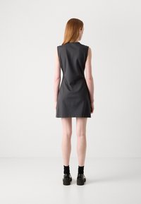 Sleeveless charcoal dress with a fitted silhouette, smooth fabric, and a hem that falls mid-thigh. Pair of chunky black shoes with black socks.