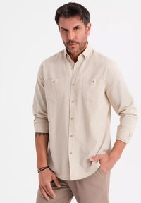 Vaahto beige pitkähihaisessa paidassa on napillinen kaulus, kaksi rintataskua, nappisuljenta edessä ja käännetyt hihat. Paita on sileäpintainen ja rento muotoilu.