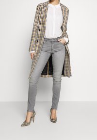 Abrigo de cuadros en amarillo, negro y blanco sobre una blusa blanca, combinado con jeans skinny grises y zapatos de tacón de serpiente.