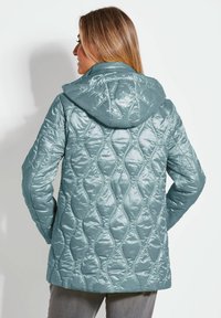 Gepolsterte türkisfarbene Jacke mit Kapuze, ausgestattet mit einem rautenförmigen Steppdesign und einer glatten, glänzenden Textur. Lange Ärmel und eine lockere Passform.