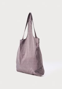 Mehka vijolična torba za na ramo z vzorcem, ki se ponavlja, in dolgimi trakovi, ima prostorno zasnovo in gladko teksturo.