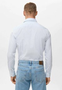 Camisa de rayas azul clara con cuello puntiagudo y puños abotonados, combinada con unos vaqueros de mezclilla azul clara de cintura alta que cuentan con un parche de cuero marrón.