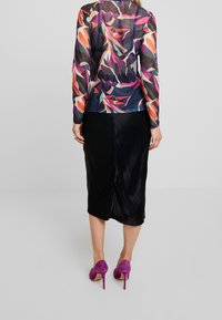 Genomskinlig långärmad topp med ett färgglatt lövmönster, ihop med en svart satinskinnkjol och lila högklackade skor.