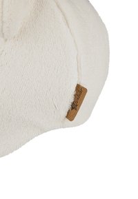 Soft, cream-colored fleece fabric close-up showing texture and a small brown fabric tag with brand name "Sterntaler" sewn into the seam.