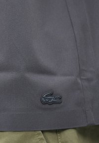 Polo shirt bleu marine avec une texture sur la surface et un accent en caoutchouc noir pour le logo en bas à gauche. Présenté avec un pantalon kaki.