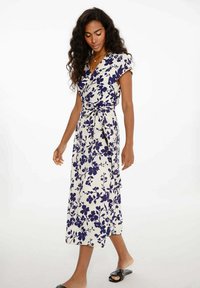 Kvetinové šaty s obojkom v krémovej farbe s námorníckymi kvetmi, krátke rukávy, viazaný pás, splývavá silueta a bočný rozparok. Hladká textúra látky.