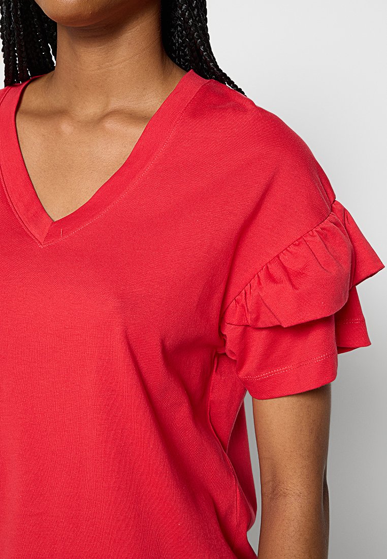 Rotes Baumwoll-T-Shirt mit V-Ausschnitt und kurzen Ärmeln, das Rüschendetails in der Schulterpartie aufweist. Sanfte Textur und einfarbig.