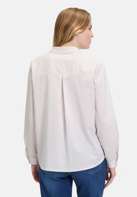 White shirt with vertical fine stripes in pale colors. Features a back yoke, long sleeves, and a buttoned cuff. Soft, textured fabric.