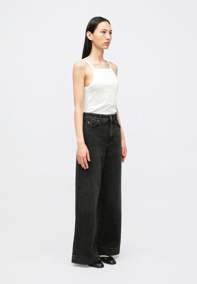 Mustad laiade jalgadega teksad kõrge vöökohaga, kombineeritud valge kitsas topiga. Sujuv tekstuur, ilma nähtavate mustriteta ja ühevärviline.