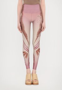 High-waisted leggings in gradient pink with floral and dotted patterns, featuring a smooth texture and a fitted design. Paired with light wooden clogs.