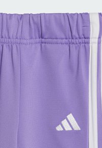 Lila sportshorts med elastisk midja, med vita sidostriper och en reflexiv vit logotyp på den nedre framen.