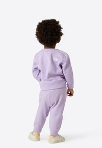 Vaaleanpunainen lasten verkkapuku, jossa on pyöreäkauluksinen paita ja kapenevat housut; takana valkoinen logo, pehmeä kangas ja resorikahvat.