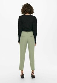 Czarna bluzka z fakturowanymi bufkami i jasnozielone, dopasowane spodnie. Slim fit z tylnymi kieszeniami, dopełnione czarnymi sandałami na wysokim obcasie.