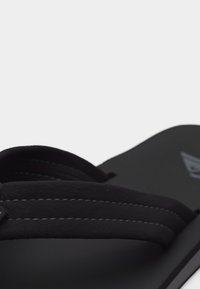 Μαύρο σανδάλι με επενδυμένο λουράκι που διαθέτει λευκές ραφές και ανάγλυφο λογότυπο της μάρκας στη σόλα.