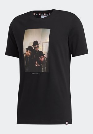 T-shirt en coton noir avec une grande impression photographique montrant quatre personnes portant des chapeaux et des chaînes, col rond standard, manches courtes.