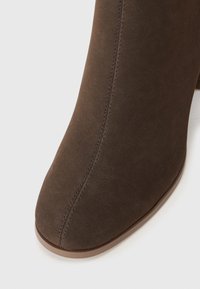Gros plan sur la pointe d'une botte en daim marron avec une couture centrale double et une semelle en caoutchouc marron clair sur fond blanc.