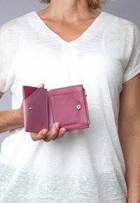 Rosa Lederbörse mit strukturierter Oberfläche, ausgestattet mit einem Druckknopfverschluss und einem Innenfach. Kompakte Gestaltung, die in der Hand gehalten wird.