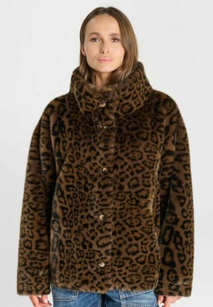 Donna che indossa una giacca marrone in pelliccia ecologica con stampa leopardata e collo alto con bottoni, abbinata a jeans blu, su sfondo semplice.
