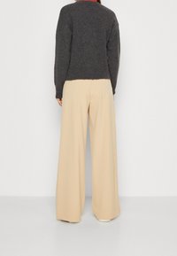 Maglione grigio a maglia con una finitura testurizzata, abbinato a pantaloni beige a gamba larga. L'outfit presenta una vestibilità rilassata e dettagli minimi.