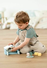 Houten speelset met een blauwe schuur, een wit dak en een zwartgeplekte koe. Inclusief twee gekleurde figuren: een roze bloem, een groene cactus en gele blokken.