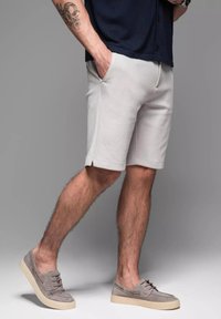 Graue Shorts aus weichem Stoff mit seitlichen Taschen, im lockeren Schnitt. Kombiniert mit hellgrauen Sneakers und einem navyblauen Shirt.