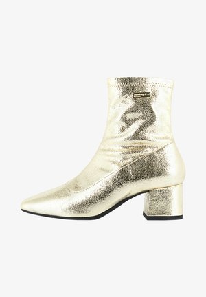 Botín metálico dorado con punta afilada, diseño elástico y tacón cuadrado. Textura suave con finos detalles en la superficie.