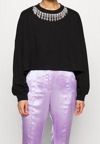 Felpa corta nera con scollatura di gioielli, maniche lunghe, abbinata a pantaloni di satin lilla chiaro.