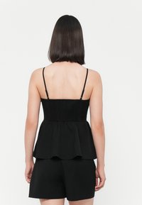 Črna peplum bluza z nastavljivimi tankimi naramnicami, smučano telo in razširjen rob. Oznaka ima mehak, gladek teksturo.