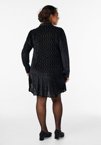 Czarna koronkowa sukienka z długimi rękawami, wzorzysty materiał i rozkloszowany dół. W zestawieniu z czarnymi rajstopami i butami na słupku.