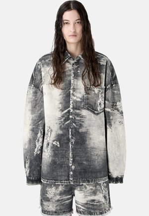 Mujer con cabello largo y oscuro que lleva una chaqueta de botones negra y gris lavada con ácido de gran tamaño y shorts a juego con detalles desgastados.