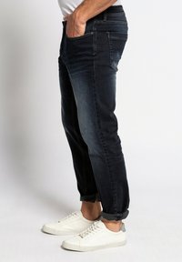 Jeans in denim blu scuro con una vestibilità slim, dotati di vita media, cinque tasche e orli arrotolati. Abbinati a sneakers bianche a bassa altura.