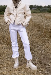 Chaqueta corta beige con una textura suave, combinada con pantalones blancos de pierna recta y botas beige con cordones y suela gruesa.