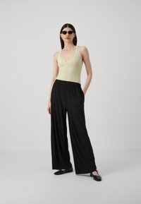 Light green ribbed tank top paired with high-waisted black pleated wide-leg trousers; model wearing black sunglasses and flat shoes.