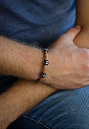 Braided tan leather bracelet with silver and black metal accents. Textured design features round metal rings between leather segments.