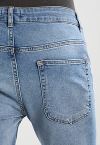 Ljust blå denimjeans med en blekt tvätt, med femfickorsdesign och förstärkt sömnad. Bakfickan är synlig med böjd sömdetalj.