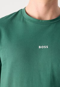 Grünes Kurzarm-T-Shirt aus Baumwolle mit Rundhalsausschnitt und weißem "BOSS"-Logo auf der linken Brustseite.