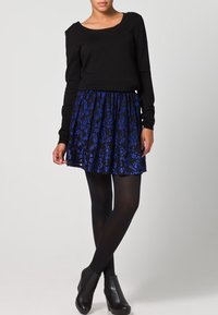 Maglia nera a maniche lunghe abbinata a una gonna corta blu con motivo floreale. La modella indossa collant neri e stivaletti con tacco.