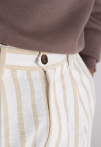 Beige og hvite stripete linbukser med knappelukking og glidelås. Lett, strukturert stoff med vertikale striper jevnt fordelt.