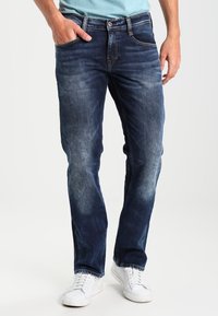 Džínové kalhoty v tmavě modré barvě s jemným vyšisovaným efektem, rovného střihu, se pěti kapsami a zapínáním na knoflík. V kombinaci s bílými teniskami.